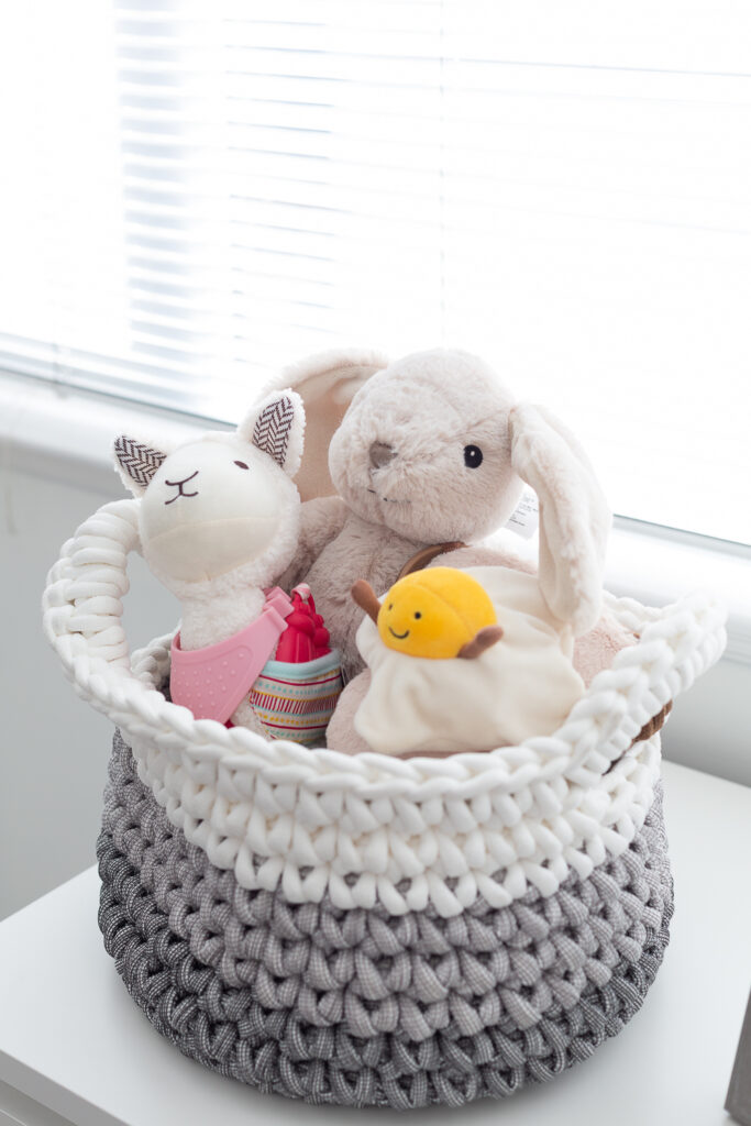 Baby storage basket with Cloud b white noise bunny, Skip Hop llama, and Jellycat Egg on Toast toy